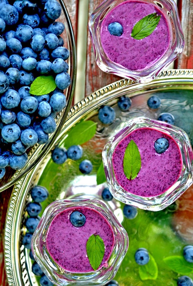 Three bowls of bluebery soup with fresh mint leaves and fresh blueberries.