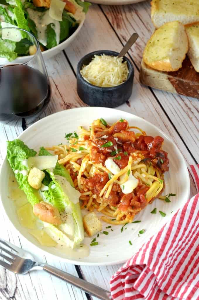 A plate of sauced spaghetti and romaine salad sitting on tble