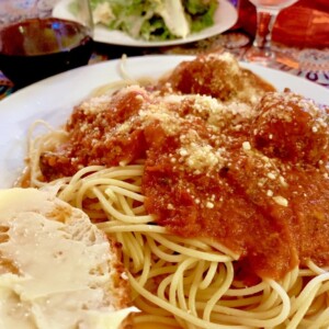 Plate of sphaghetti and meatballs with hoemade bread and caesars salad.