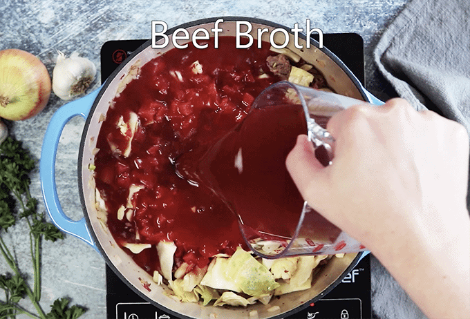 Beef broth being added to pot of cabbge