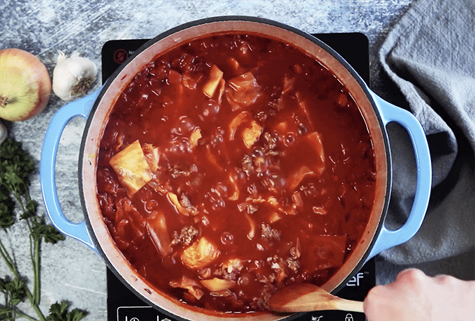 Pot of cabbage and tomato sauce being stirred with wooden spoon