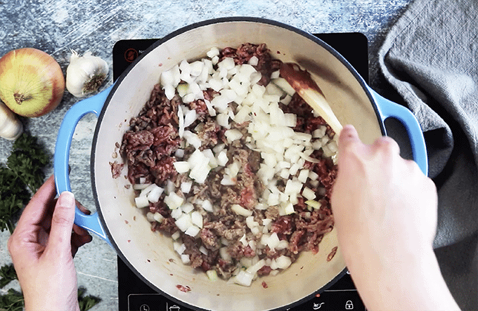 Person stirring meat and onions in pan