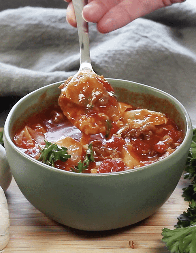 A bowl of soup on a wooden table with soup in spoon