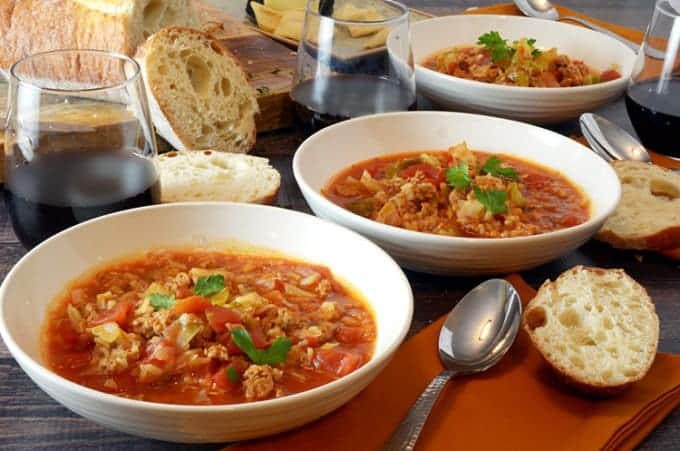 3 bowls of cabbage soup on table with bread and spoon