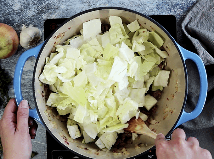 Person stirring cabbage in pot with wooden spoon