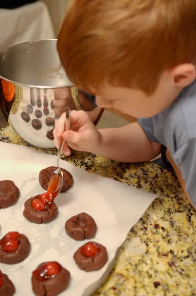 A boy adding cherries to chocolate cookies