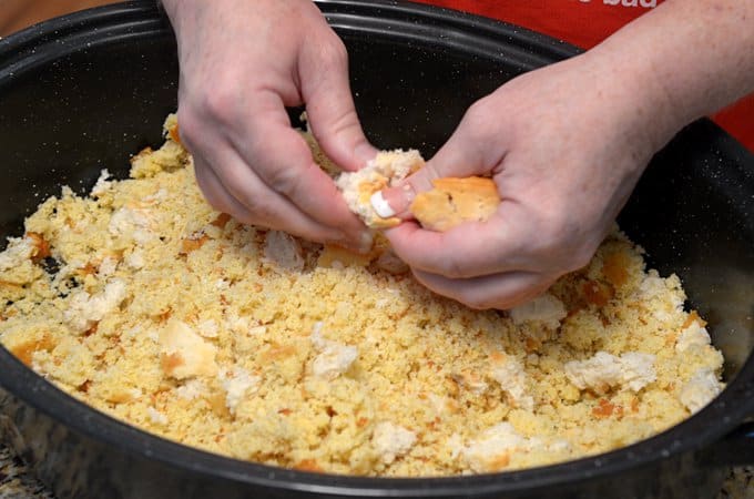 A pair of hands breaking up cornbread in a slow cooker