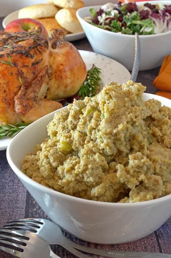 Bowl of cornbread dressing with roasted chicken and salad in the background.