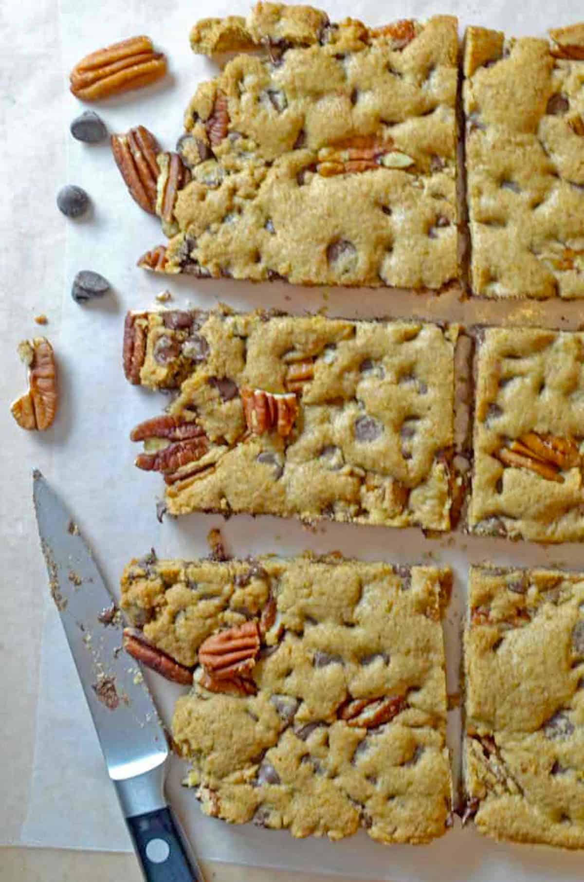 Overhead view of a knife and some cut-out pecan bars on parchment paper.