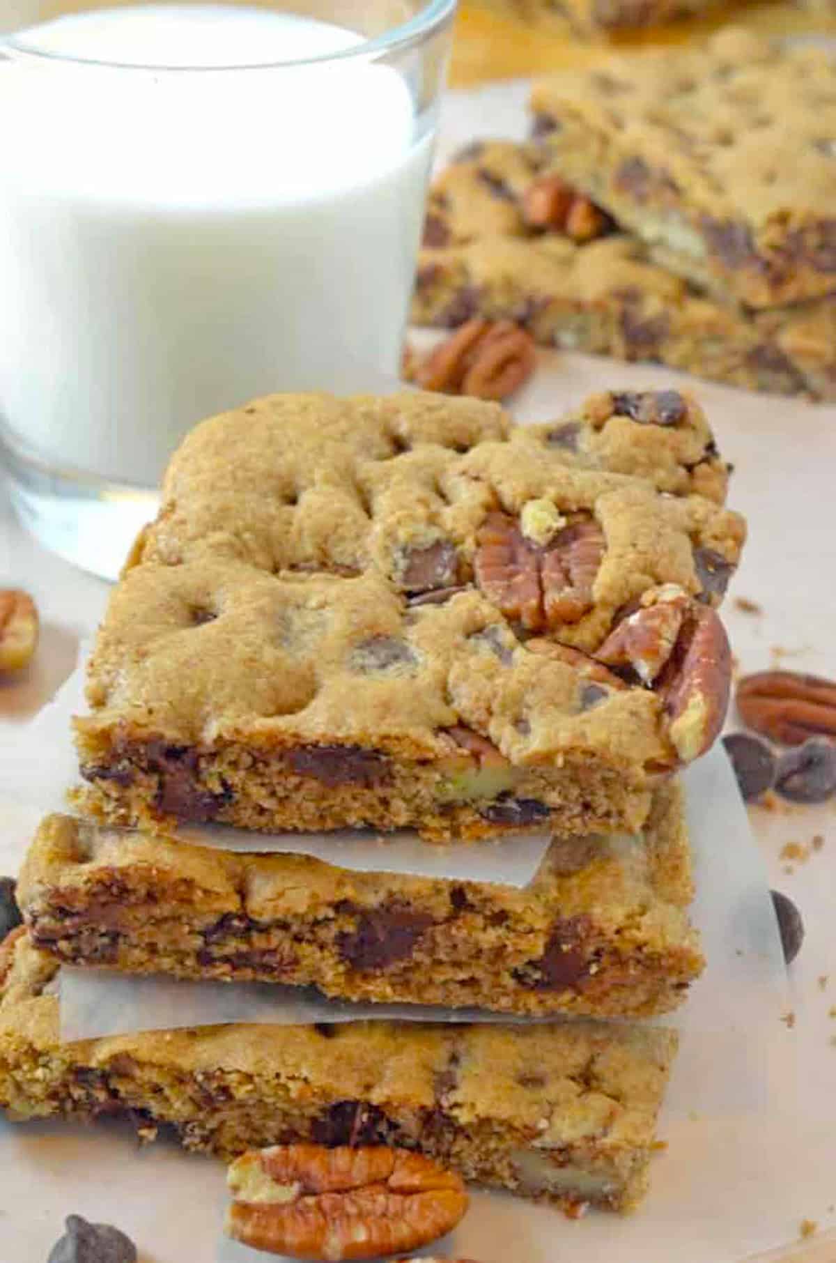 A stack of chocolate chip pecan bars with a glass of milk.