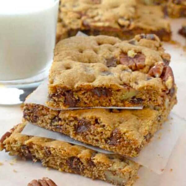 A stack of dessert bars with a glass of milk.