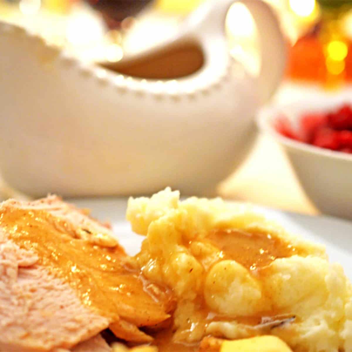 Mashed potatoes with turkey gravy and roasted turkey on a plate.