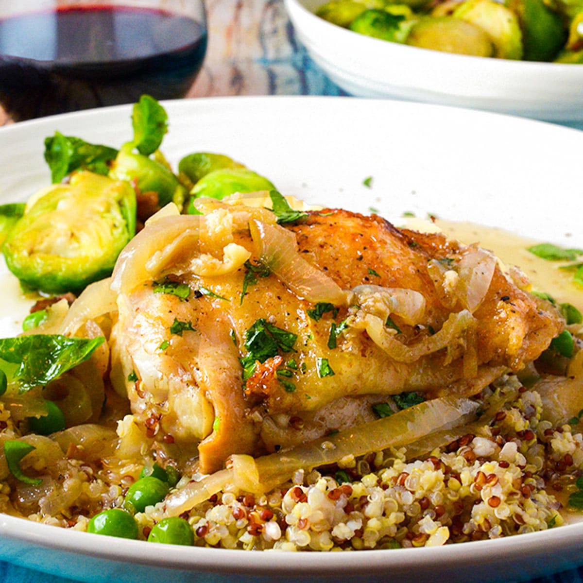 Seared chicken thigh on a serving plate with quinoa and Brussels sprouts.