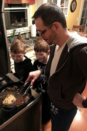 A man cooking food in a kitchen, with two young boys