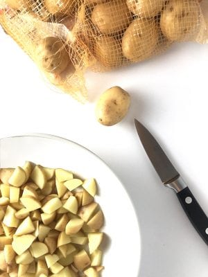Bag of potatoes and knife with dish of cubed potatoes.