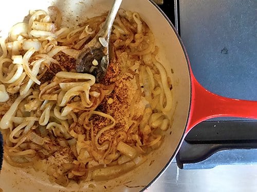 Onions being caramelized in saute pan with wooden spoon