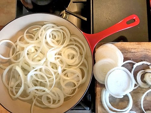 Raw onion cuts in saute pan and cutting board