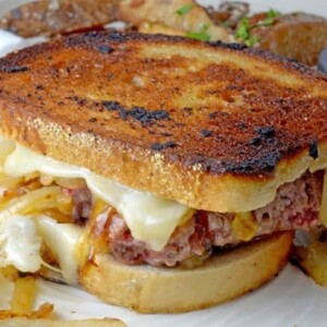 Whole grilled sandwich with meat, cheese and caramelized onion on plate