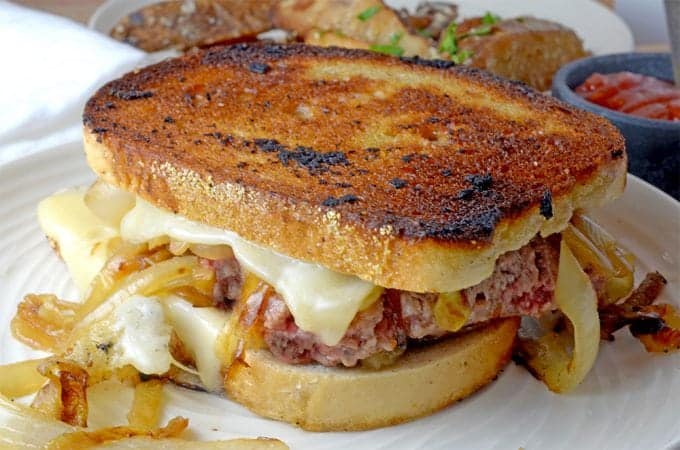 Whole grilled sandwich with meat, cheese and caramelized onion on plate