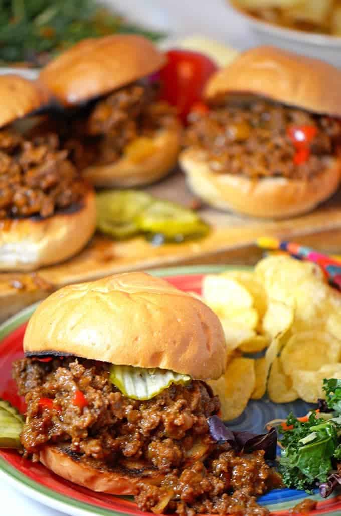 3 Sloppy Joe Sandwiches on board behind plated Joe with chips