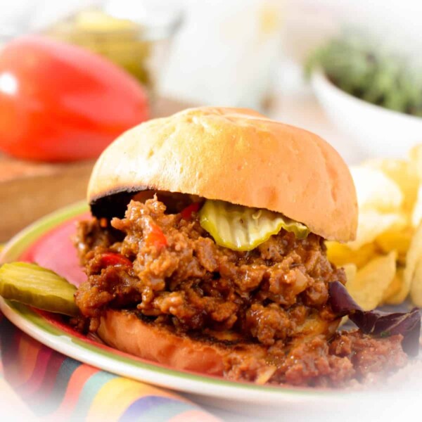 Sloppy Joe sandwich with picke and chips on a white plate.