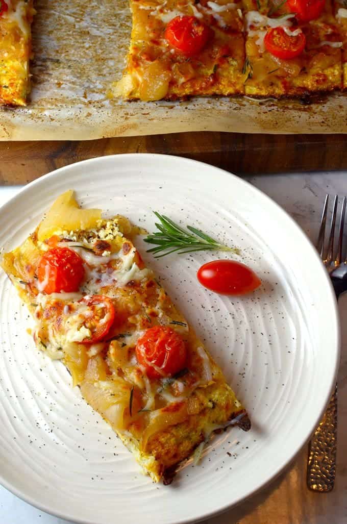 A plate with a cauliflower latke and cherry tomato with rosemary garnish