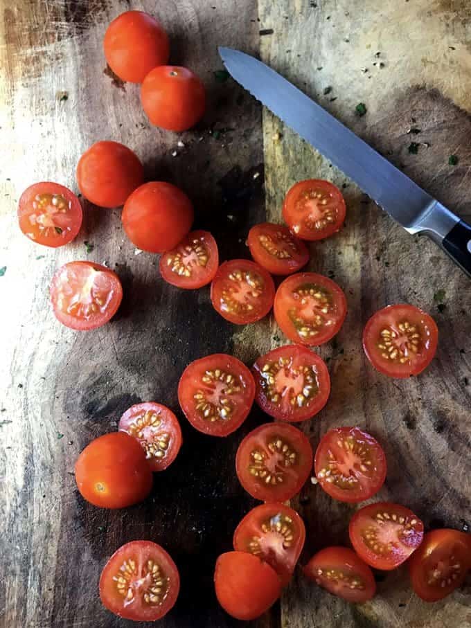 Sliced cherry tomatoes on a cutting board with a serrated knife.