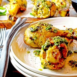 Two chicken drumstricks on a plate with chimichurri sauce.