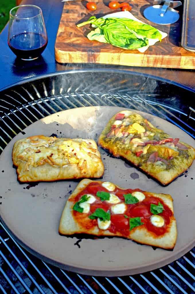 A pizza stone on bbq grill cooking 3 types of pizza