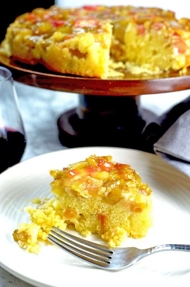 Serving of rhubarb upside-down cake on a plate with whole cake in the background.