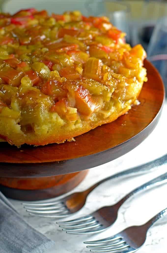 Cake topped with rhubarb on a serving platter with three forks.