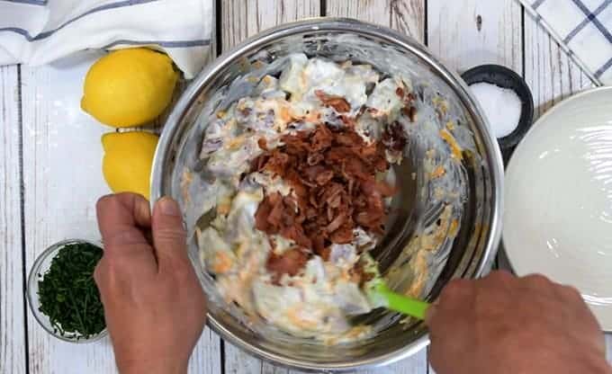 A person stirring bacon into potato ranch salad