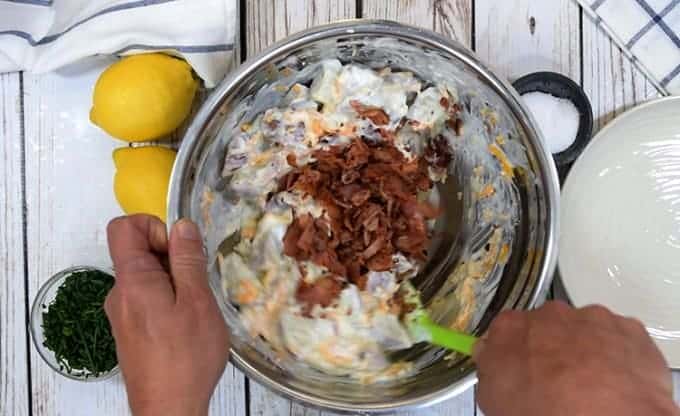 A person stirring bacon into potato ranch salad 