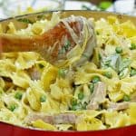 A wooden spoon stirring a skillet of noodles