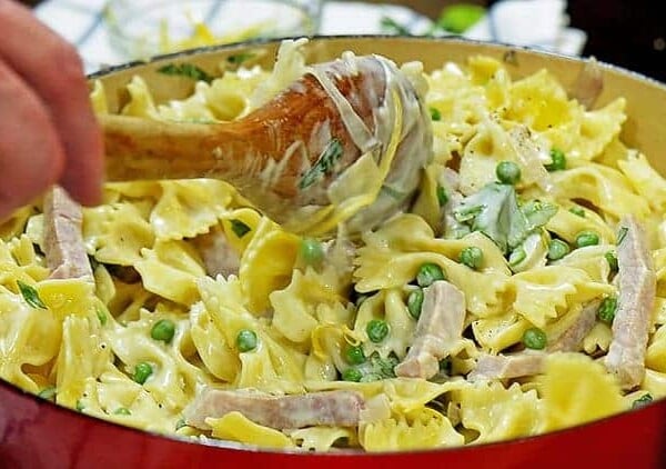 A wooden spoon stirring a skillet of noodles