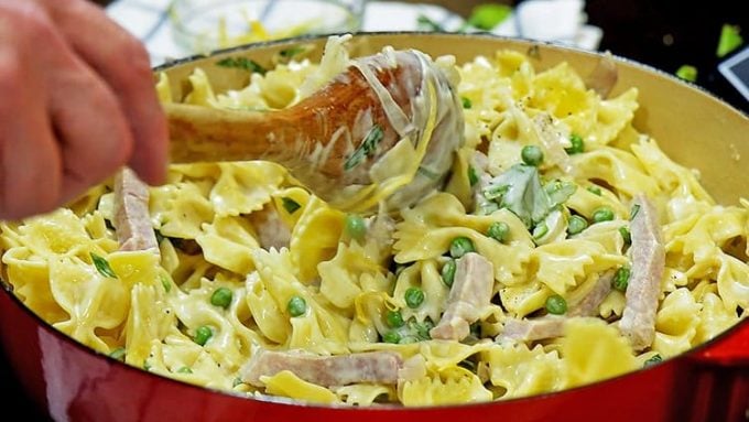 A wooden spoon stirring a skillet of noodles