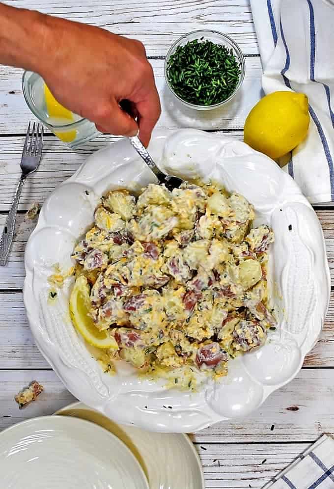 A person holding a plate of food with a knife, with potato salad