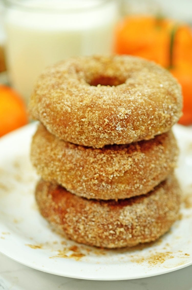 Three pumpkin donuts stacked on a plate with a glass of milk