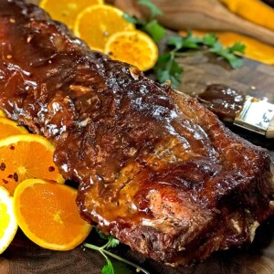 Glazed ribs with sliced oranges, pastry brush and wooden spoon on board