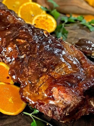 Glazed ribs with sliced oranges, pastry brush and wooden spoon on board