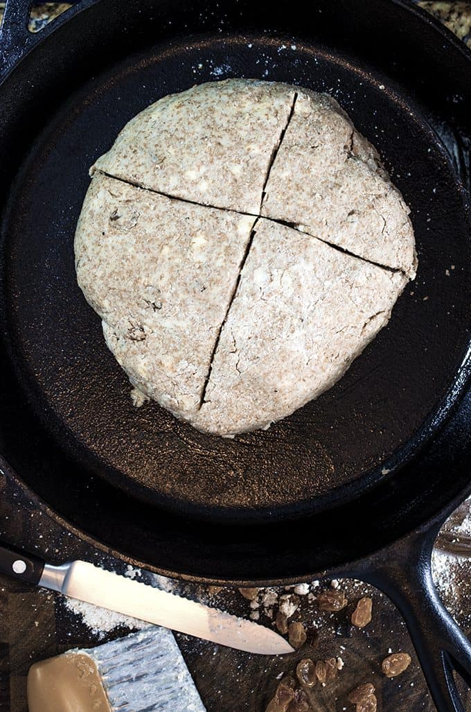 Iron skillet containing raw round of bread with cut cross on top