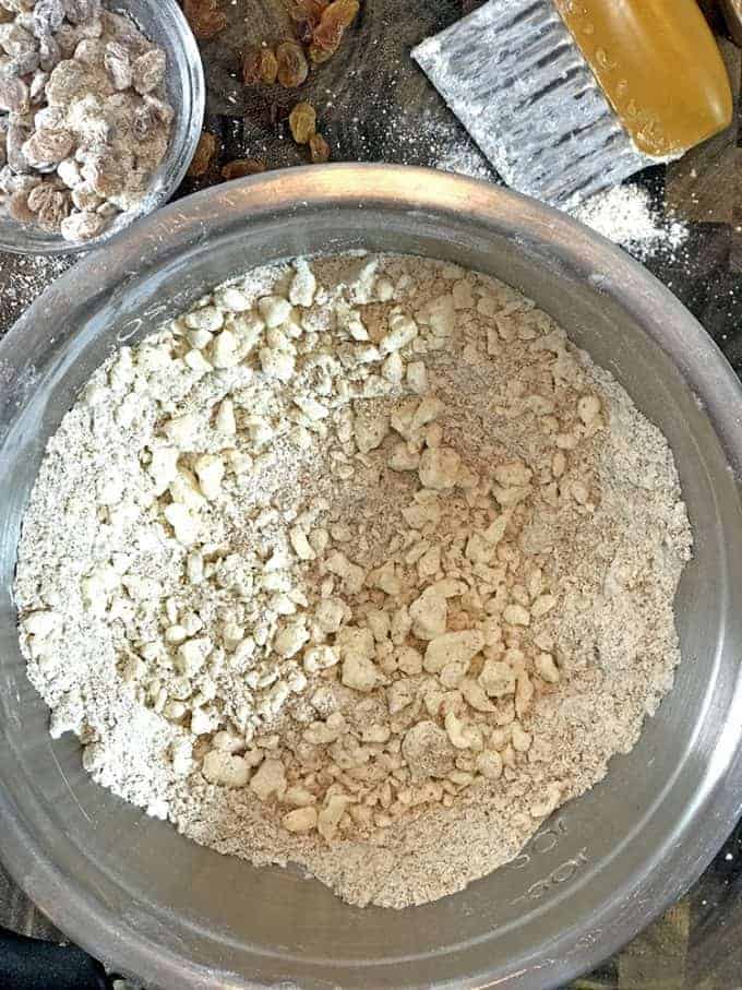 Flour crumbs in stainless bowl next to floured raisins in bowl