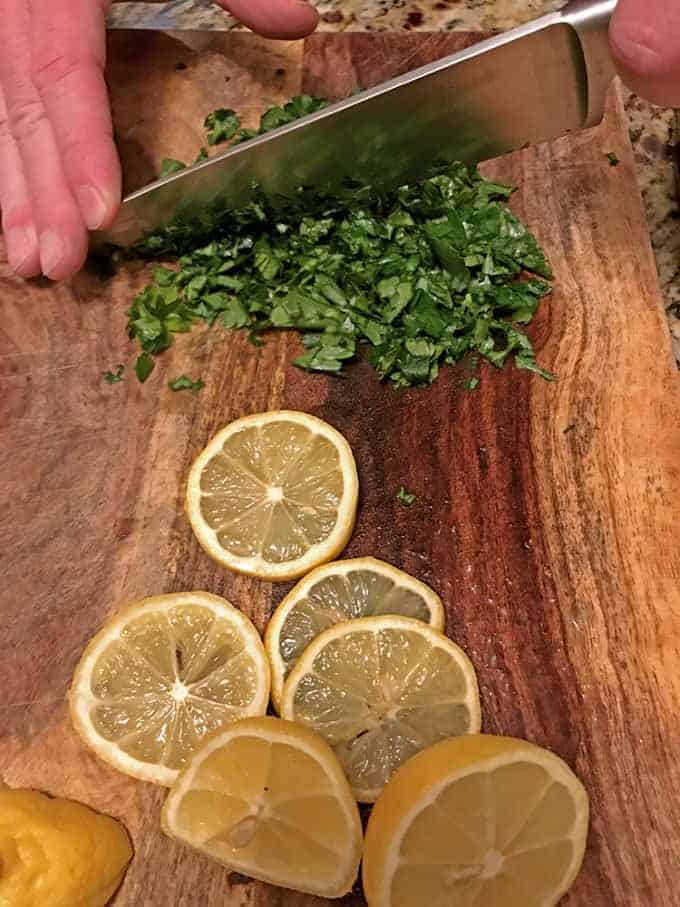 Someone chopping parsley on cutting board nest to sliced lemons