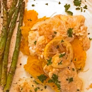 Chicken breast atop shredded squash, asparagus on side with lemon on top