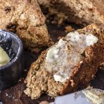 Close up piece of buttered whole wheat Irish soda bed with loaf in back