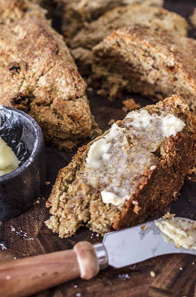 Close up piece of buttered whole wheat Irish soda bed with loaf in back