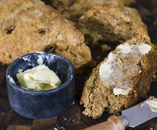 Crock of butter next to buttered slice of bread and loaf on board