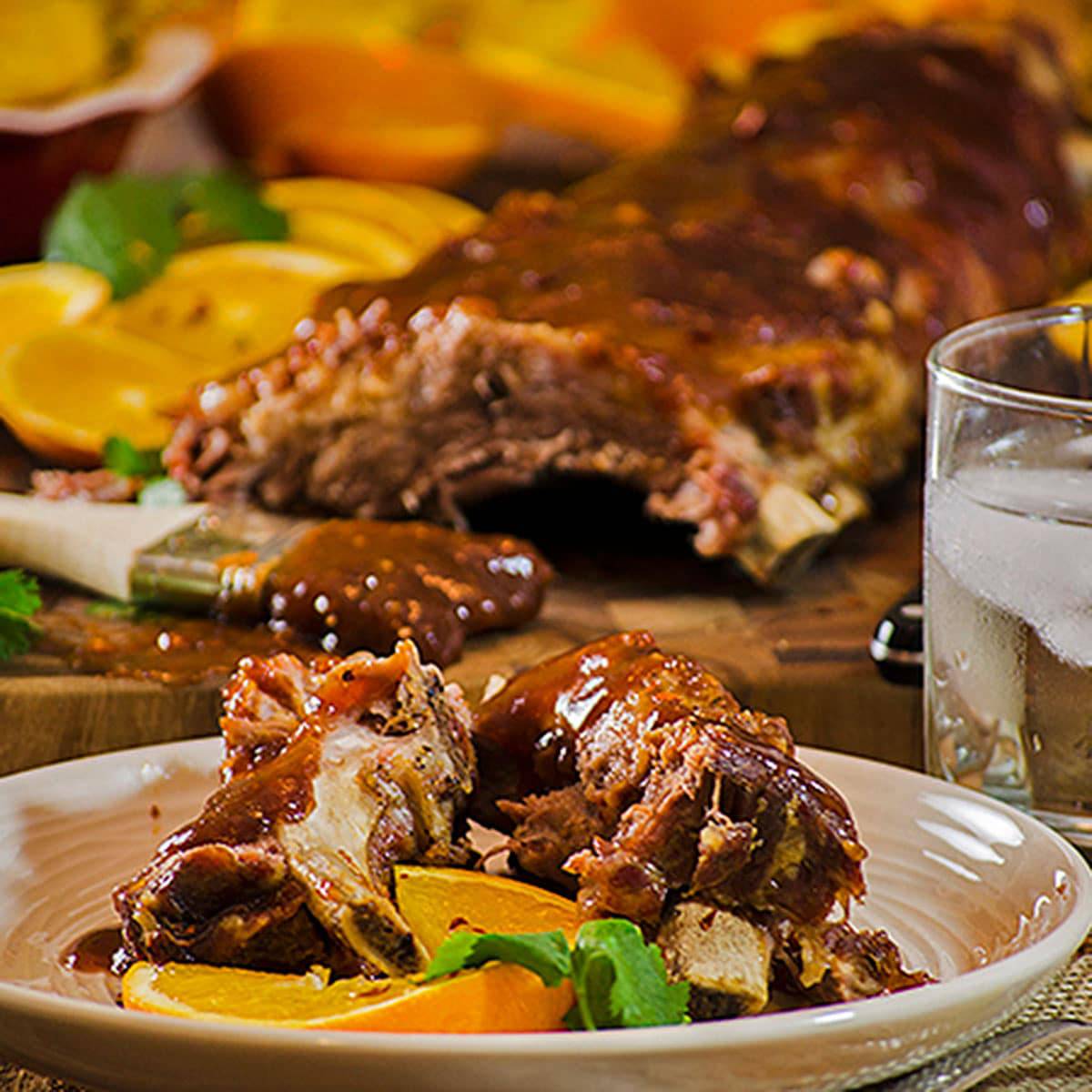 A plate full of ribs cut from slab with oranges in background on board