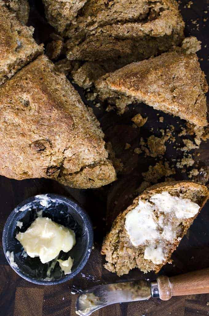 Loaf of brown bread with cut, buttered piece on board next to butter