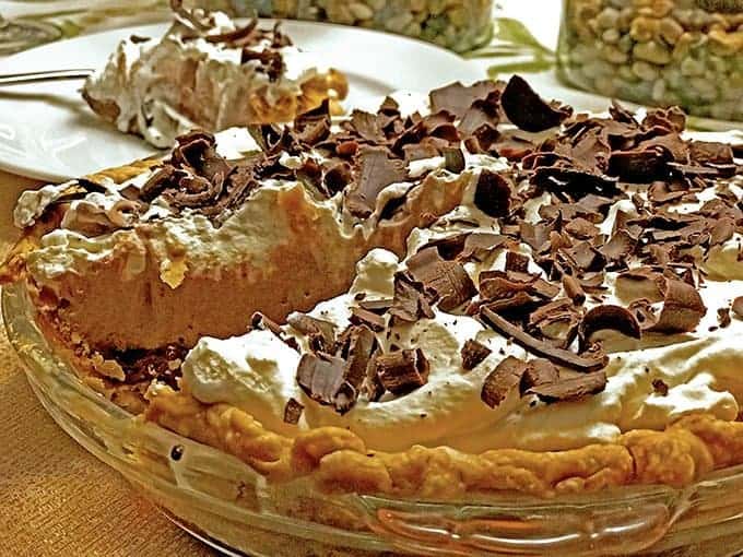  Chocolate cream pie with one slice removed on plate, behind pie dish